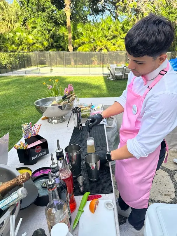 Bartender in a pink apron mixing a drink outdoors.